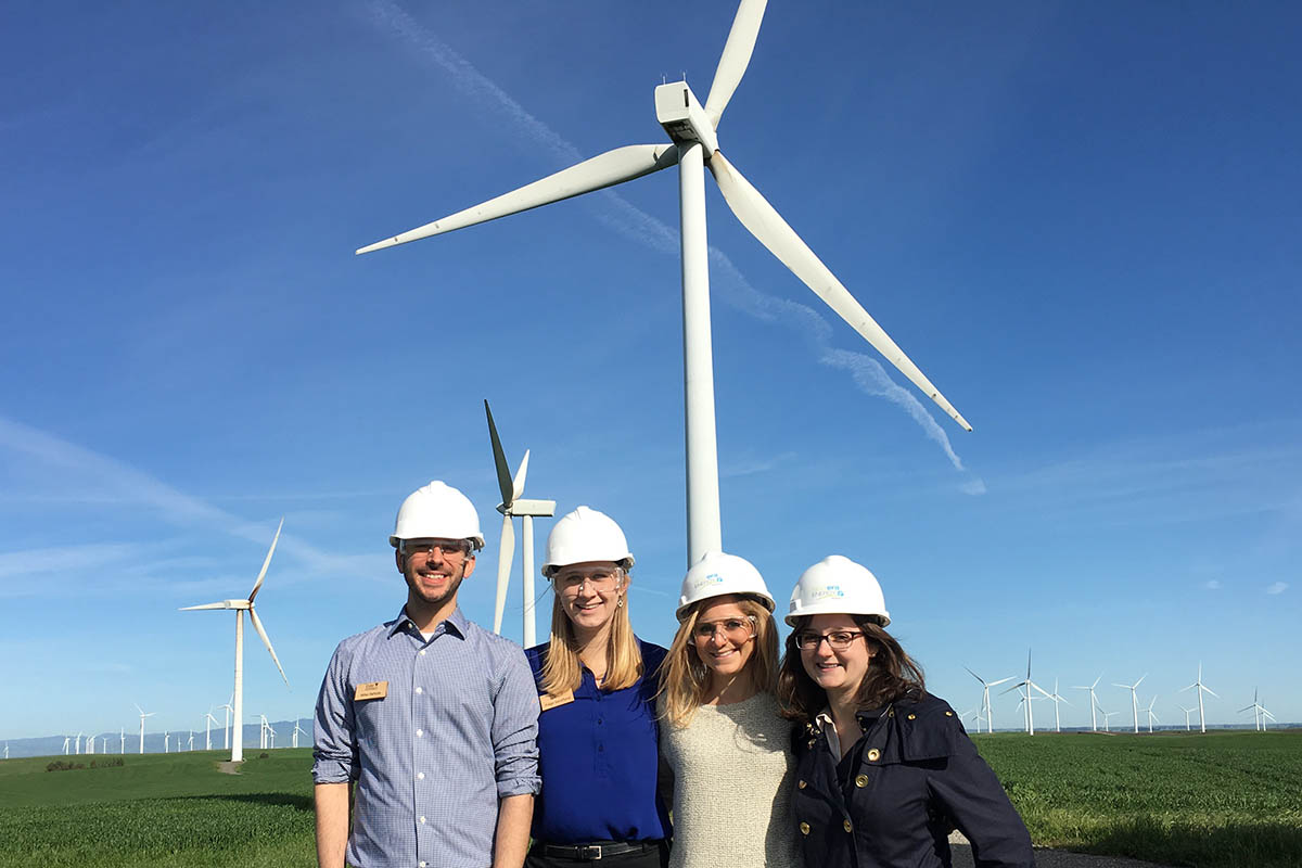 Four students wearing hardhats in a wind farm
