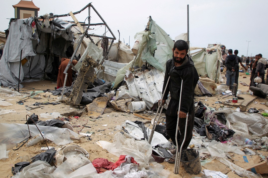 فلسطيني يستند إلى عكازه وسط خيام دمرتها قذائف الاحتلال الإسرائيلي في رفح - رويترز