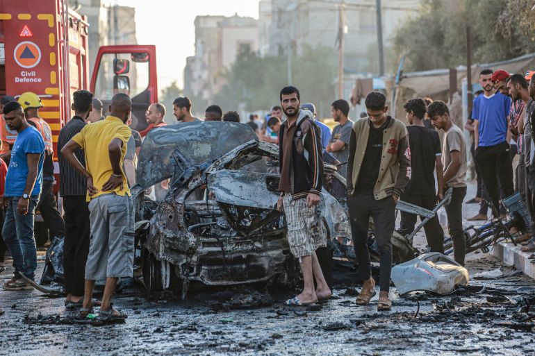 Palestinians check a burnt vehicle following an Israeli strike in the central Gaza Strip