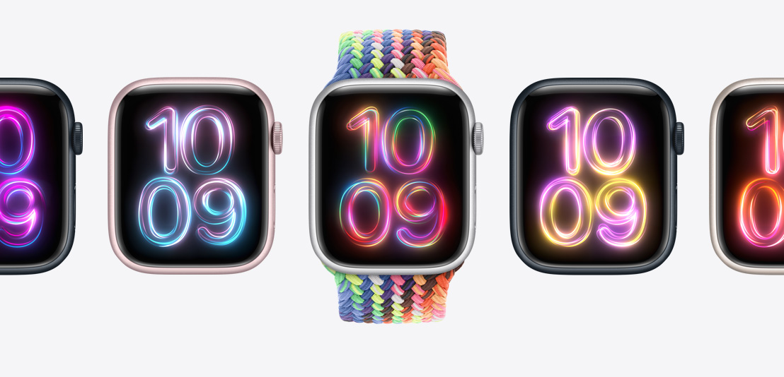 Hodinky Apple Watch Series 9, prostřední hodinky s novým pleteným navlékacím řemínkem Pride Edition v neonových barvách, ciferník Pride Radiance na každých hodinkách v jiných barvách.