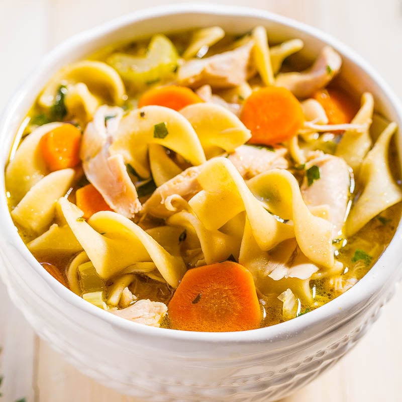 A bowl of chicken noodle soup with carrots, celery, and herbs.