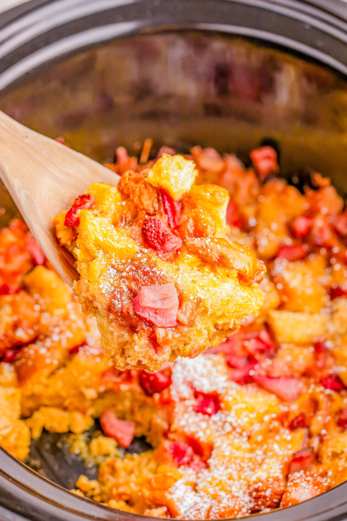 A spoon lifts a serving of bread pudding with chunks of ham from a pot, containing a mixture of fruit and dough with visible pieces of ham.