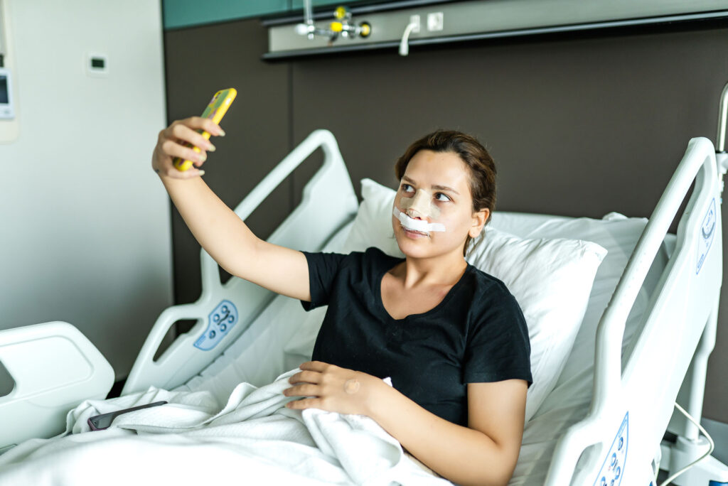 Photo: A picture of a woman who has bandages on her nose taking a selfie on her phone
