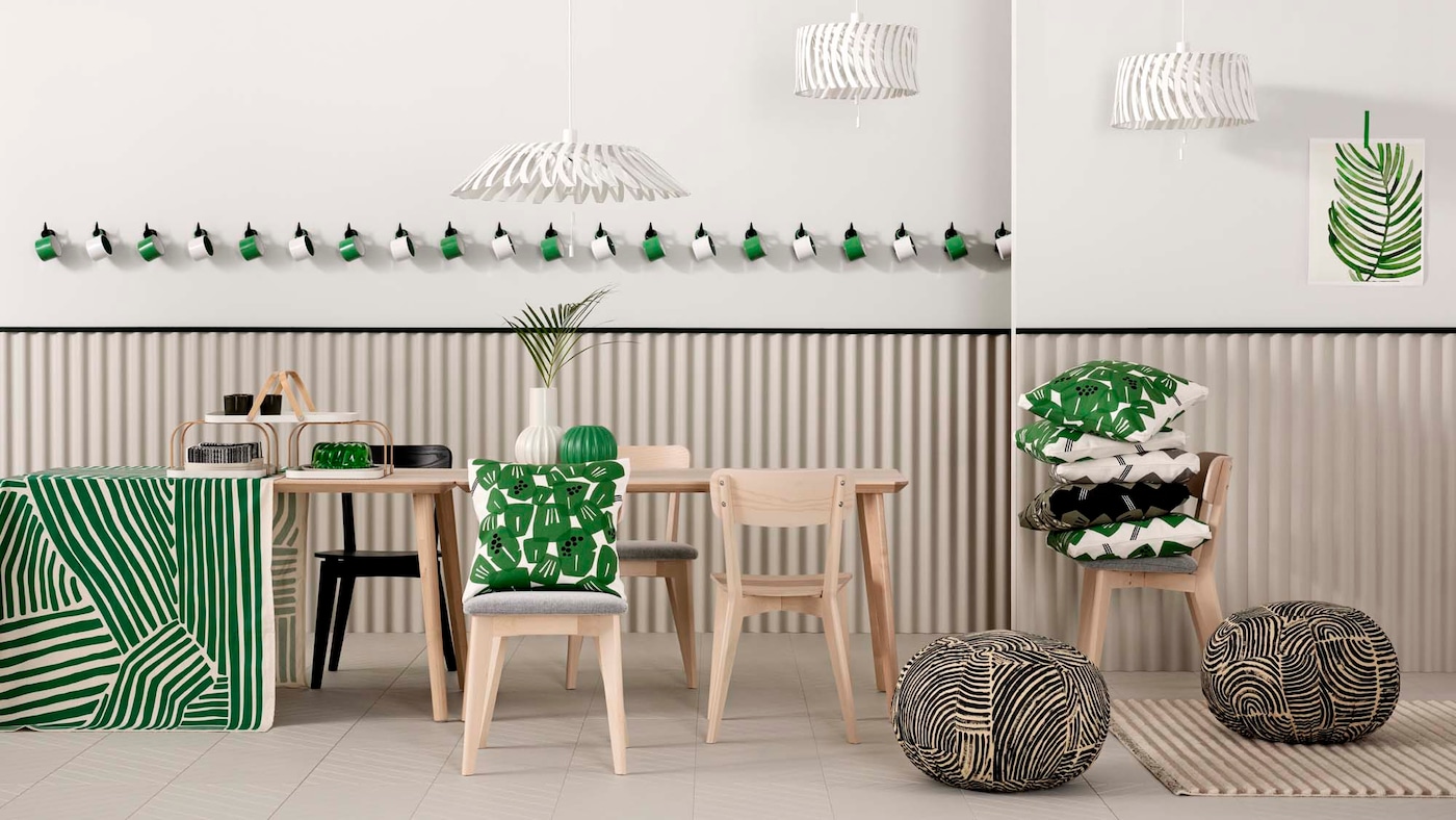 A dining room table and chairs stacked with green, black and white cushions, against a striped background.
