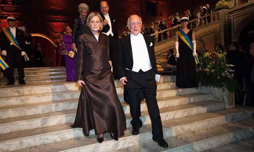 Peter Higgs and Mrs Marci Hazard, spouse of Chemistry Laureate Martin Karplus, proceed down the stairs into the Blue Hall. 