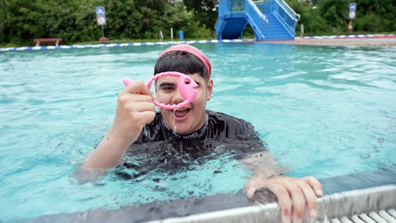 Schüler Khalil-Abdul hält stolz einen Ring in die Höhe während er im Schwimmbecken ist. © NDR Foto: Screenshot