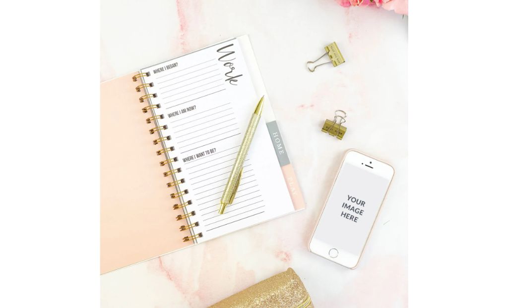 Open notebook with pen on top next to a cell phone with pastel accents