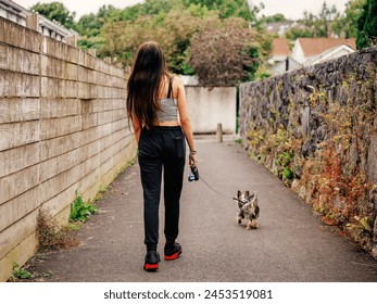 Teenager girl with walking with small cute Yorkshire terrier in a street. Taking care of your pet concept. Outdoor activity. Model with slim body type and long rich hair. 库存照片
