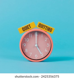 the text quiet quitting written on two yellow rectangular pieces, on a pink clock striking five, on a blue background Foto Stock