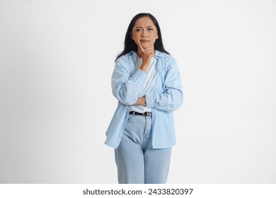 Una reflexiva mujer asiática que viste camisa azul está imaginando sus pensamientos, aislados por el fondo blanco. Foto de stock