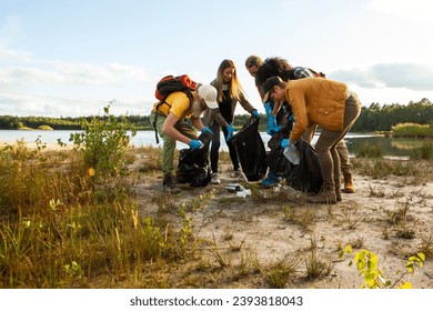 Esta imagen captura un grupo de individuos que participan activamente en una limpieza a orillas del lago. Vestidos con atuendos casuales al aire libre y armados con bolsas de basura y guantes, están doblados, recogiendo basura Foto de stock