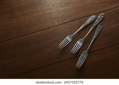 Three old silver forks with ornate carvings on the handles on a wooden motif background 库存照片