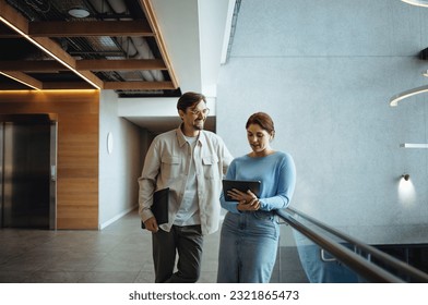Two business professionals standing together, discussing and using a digital tablet. Happy business colleagues, a man and a woman, cooperating for the growth and success of their company.: stockfoto
