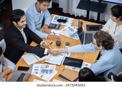 Стоковая фотография: Two businessman shake hand in meeting room with coworker give cheerful applause. Team of analyst celebrate after successful significant progress on business strategic performance. Meticulous