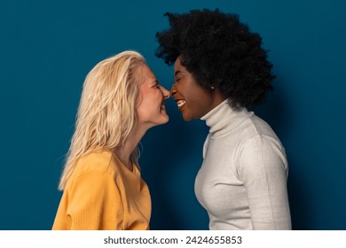 青の背景にスタジオで鼻をこする2人の多民族の女性の友人。の写真素材
