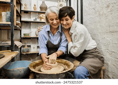 Two women, a mature lesbian couple, work together at a pottery wheel in a cozy art studio.の写真素材