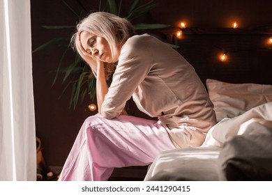 動揺した中年の女性が寝室でベッドに座って問題解決を考え込んで失われ、落ち込んだ不幸な成熟した女性の距離を見て、うつ病に苦しんでいますの写真素材