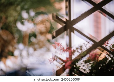 ラトビア ヴァルミエラ - 2024年7月28日 – 女性の反射が格子と花のパターンによって重ね合わされた窓に見られます。の写真素材