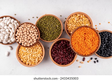 様々な乾燥豆、レンズ豆、緑豆、ひよこ豆、木製のボウルにエンドウ豆の品揃え。白いテーブルの上面ビューにマメ科植物。ビーガンタンパク質源の食品、コピー空間の写真素材