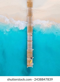 優美な青い水と波に囲まれた木製の桟橋に黄色のカヤックと黒い袋の垂直空撮グレースベイビーチの白い砂浜に墜落の写真素材