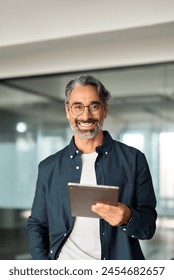 Vertical portrait of happy smiling older business man executive standing in office using digital tablet. Middle aged businessman manager wearing shirt glasses working on professional financial project Foto stock