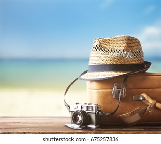 Vintage suitcase, hipster hat, photo camera and passport on wooden deck. Tropical sea and sandy beach a in background. Summer holiday traveling design concept. Stock Photo