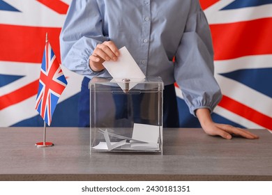 Voting young woman with UK flag near ballot box on table at polling station Arkistovalokuva