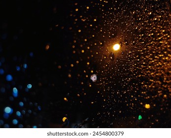 warm and cool toned lights seen through raindrops on a car window in the night sky Foto Stock