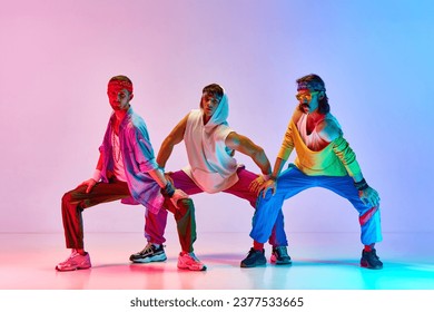 Warming-up. Men in colorful, stylish, vintage sportswear training against gradient pink blue background in neon light. Concept of sportive and active lifestyle, humor, retro style. Ad Foto Stock