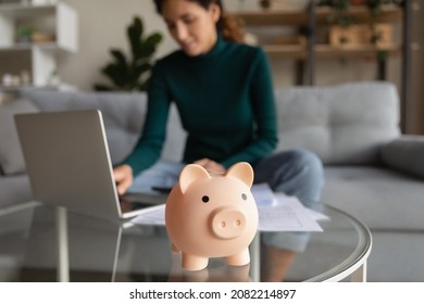 賢い経済。家計を計画する家計を計画する家計の若い女性が、ノートパソコンでアプリを使って公共料金を支払っている、ぼやけた写真。テーブルの上の、おかしなピンクのピギーバンクのおもちゃにフォーカスの写真素材