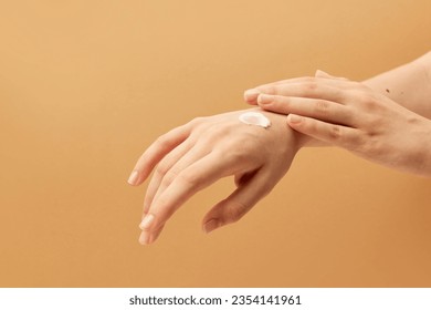 Woman taking care after hands, applying cream on her hands on beige background. Concept of body and skin care, spa, dermatology, treatment. Anti-aging. Copy space for ad 库存照片
