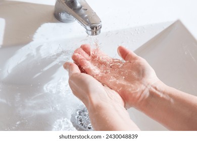 女性はエアレータなしで古いクレーンの下で手を洗い、あまりにも多くの水を使います。美しい水流と滴の接写の写真素材