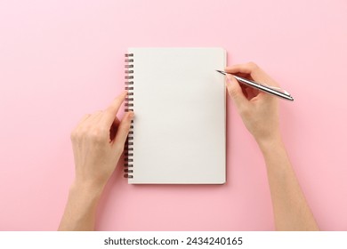 Woman writing in notebook on pink background, top view
