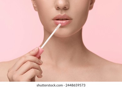 ピンクの背景に唇の光沢を適用する女性、接写の写真素材