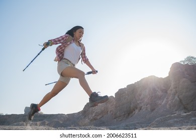 woman hiking in the mountains standing on rocky summit ridge with backpack and pole looking out over landscape. 
Active brave tourist jumping through cliff in mountain lifestyle outdoor journey. Foto stock