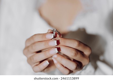 A woman is holding a ring in her hand. The woman is wearing a white dress and has her nails painted. Concept of love and commitment Foto stock