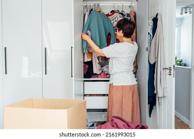 Woman selecting clothes from her wardrobe for donating to a Charity shop. Decluttering, Sorting seasonal clothes and Cleaning Up. Reuse, second-hand concept. Conscious consumer, sustainable lifestyle Stock Photo