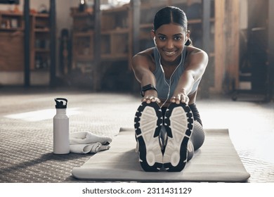 Woman is stretching legs in gym, fitness and smile, start workout with earphones, portrait and sport preparation. Health, active with happy Indian female warm up and ready for exercise with music Foto Stock