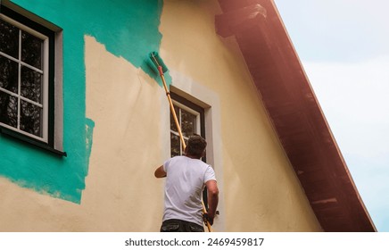 A worker paints the facade walls of a house with paint using a paint roller 库存照片