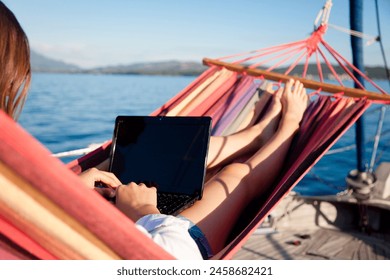 Working in traveling by sea in beach hammock. Woman with laptop on yacht. Student girl in summer vacation. Freelancer workplace outdoors. Distance learning, online education. Computer blank screen Adlı Stok Fotoğraf