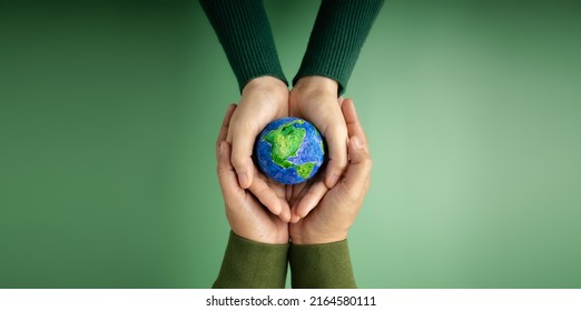 World Earth Day Concept. Green Energy, ESG, Renewable and Sustainable Resources. Environmental Care. Hands of People  Embracing a Handmade Globe. Protecting Planet Together. Top View Stock Photo