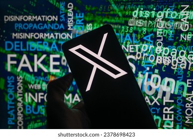 スマートフォンに表示されたXのソーシャルメディアアイコンのロゴと、背景に見える画面の偽情報、この写真イラスト。2023年10月15日、ベルギーのブリュッセルにて。のエディトリアル写真素材