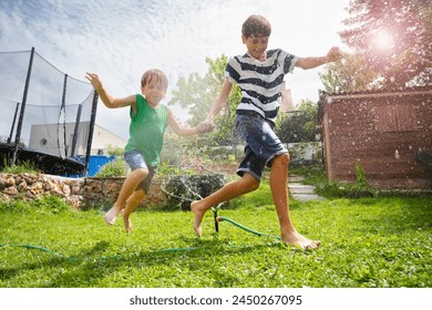 Youngsters, teen and kid, siblings enjoying a splashy game outdoors, with sunlight filtering through the water droplets at summer garden 스톡 사진