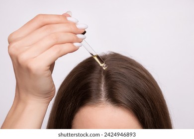A young woman applies a drop of oil from a pipette to her scalp, close-up. Vitamins, keratin for treatment, strengthening and growth of hair. Problems with dandruff, hair loss. Hair care concept, fotografie de stoc