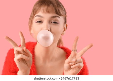 Young woman with chewing gum showing victory gesture on pink background, closeup Stock-foto