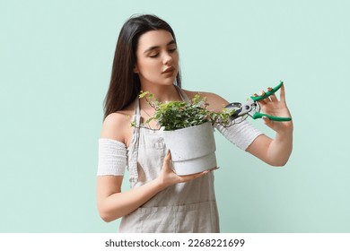 Young woman cutting houseplant with pruner on green background Stock Photo
