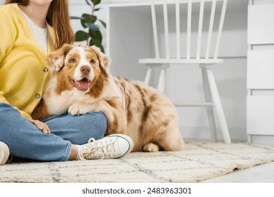 Jeune femme avec un mignon chien de berger australien assis par terre à la maison : photo de stock