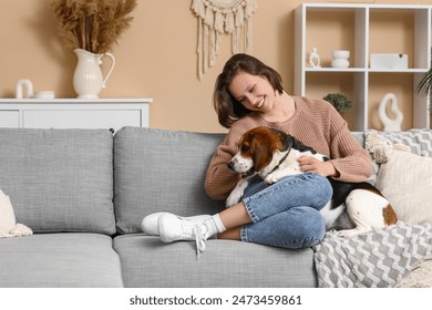 Young woman with cute Beagle dog sitting on comfortable sofa at home Arkistovalokuva