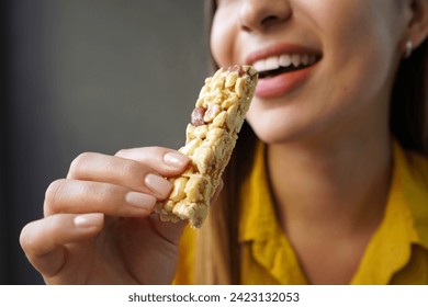 Young woman eating a nuts cereal bar without sugar on gray background Stock-foto