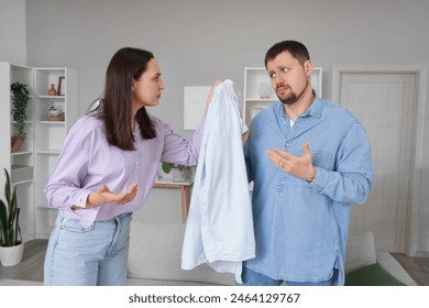 Young woman with lipstick kiss marks on her husband's shirt at home. Cheating concept Arkistovalokuva